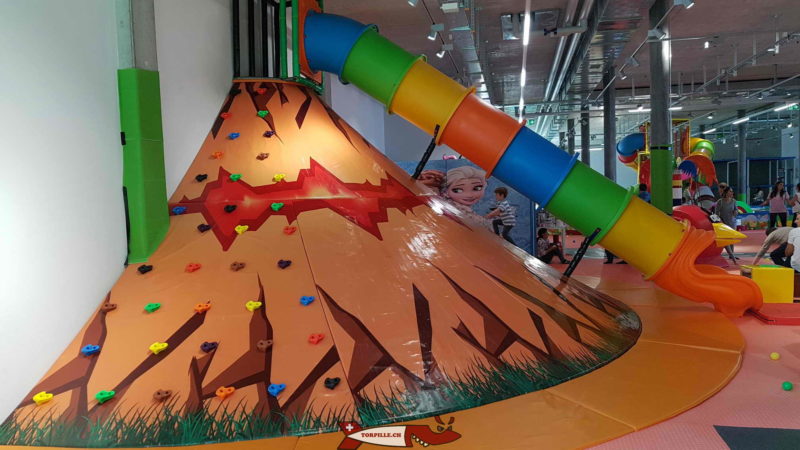 Un long toboggan multicolore accessible en montant au sommet du volcan à Kids Fun Park Etoy