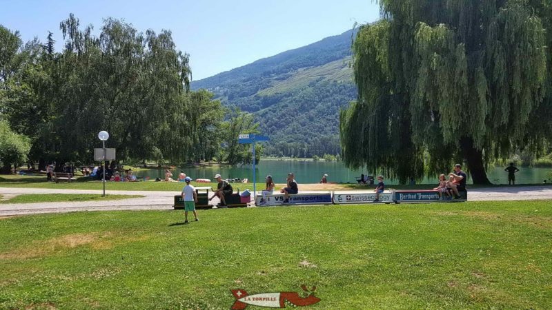 Le petit train longeant le bord du lac dans lequel se baigne des nageurs.