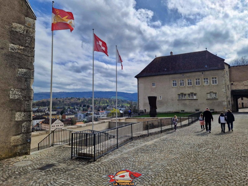 Le corps de garde avec, sous les drapeaux, l'esplanade depuis laquelle on profite d'une jolie vue sur la ville de Porrentruy.