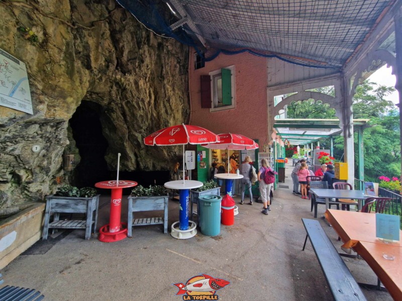 L'entrée de la grotte sur la gauche et, au milieu, contre la paroi rocheuse, le restaurant et buvette.