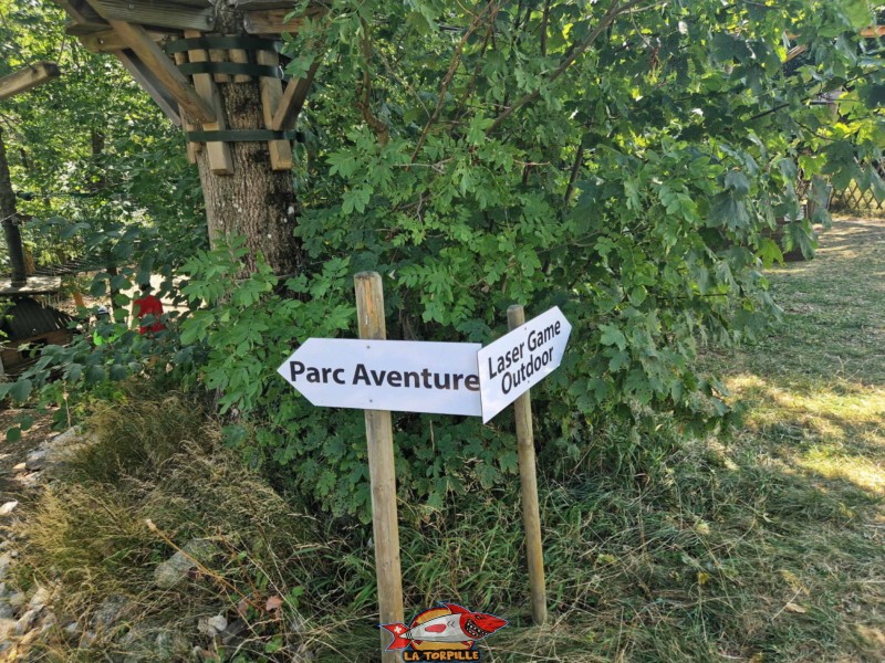 Un panneau indicateur à l'entrée de la forêt montrant le chemin vers le Parc Aventure et celui vers le laser game.