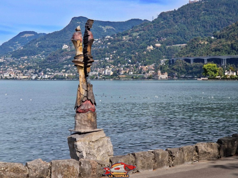 Une sculpture en forme de pièce du jeu d'échecs au bord du lac. En arrière-plan, le fameux château de Chillon et le viaduc autoroutier.