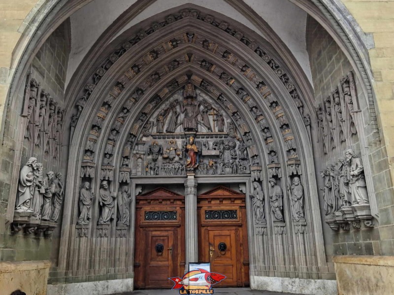 Le portique d'entrée est construit à la fin du 14ᵉ siècle et est orné de sculptures en pierre. Il représente le jugement dernier. Cathédrale St-Nicolas de Myre, Fribourg.