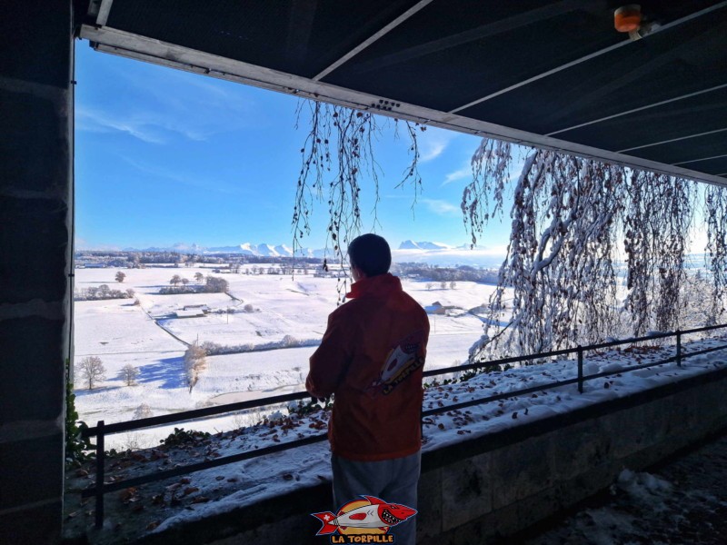 La vue, en hiver, sous la passerelle, sur les Préalpes fribourgeoises avec le Vanil Noir et le Moléson. Le Vitromusée de Romont ou musée suisse du vitrail et des arts du verre