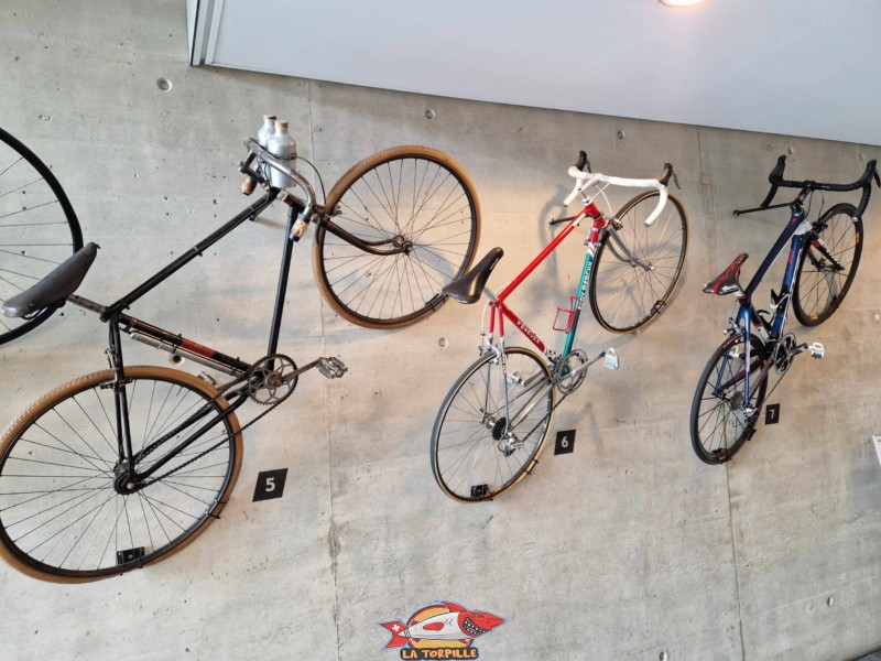 À gauche, années 1910, un vélos des premières compétitions cyclistes. Au milieu, un vélo des années 1980 avec un changement de vitesse sur le cadre. À droite, un vélo de dernière génération. Cadre et roues en carbones, pédales automatiques, changement de vitesse sur le levier des freins. Centre mondial du Cyclisme (CMC) de l'UCI (Union Cycliste international) à Aigle, canton de Vaud.