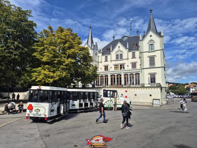 Le petit train à son point de départ à la place du Marché de Vevey avec le château de l'Aile. Le petit train à son point de départ à la place du Marché de Vevey avec le château de l'Aile.