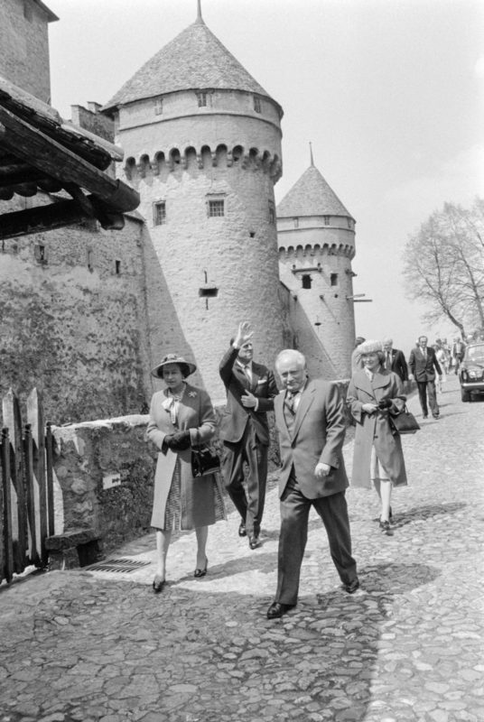 La reine du Royaume-Uni en visite au château en 1980. Son mari, le prince Philipp, est juste derrière elle le bras levé.