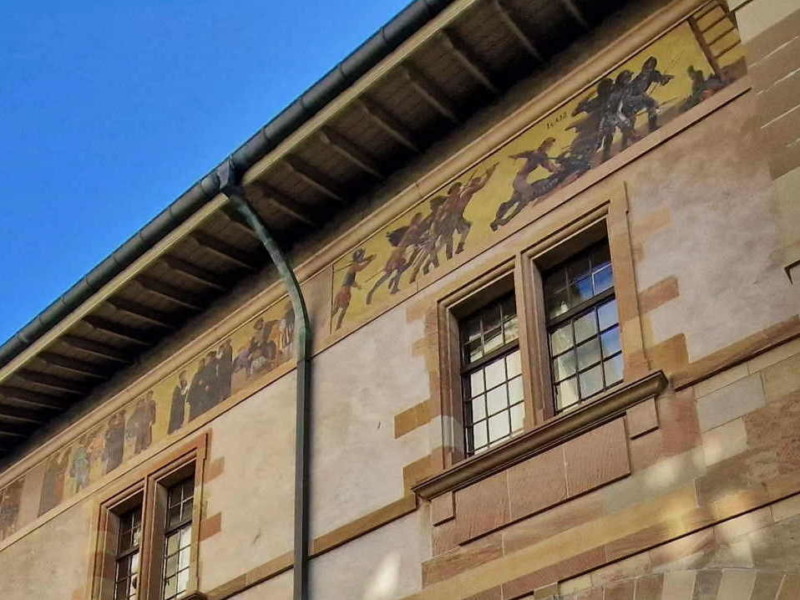 Une partie de la frise sur le côté ouest de l'ancien arsenal, juste sous la toiture avec deux évements majeurs de l'histoire de Genève. A gauche, l'instauration de la Réforme et l'Escalade, sur a droite.