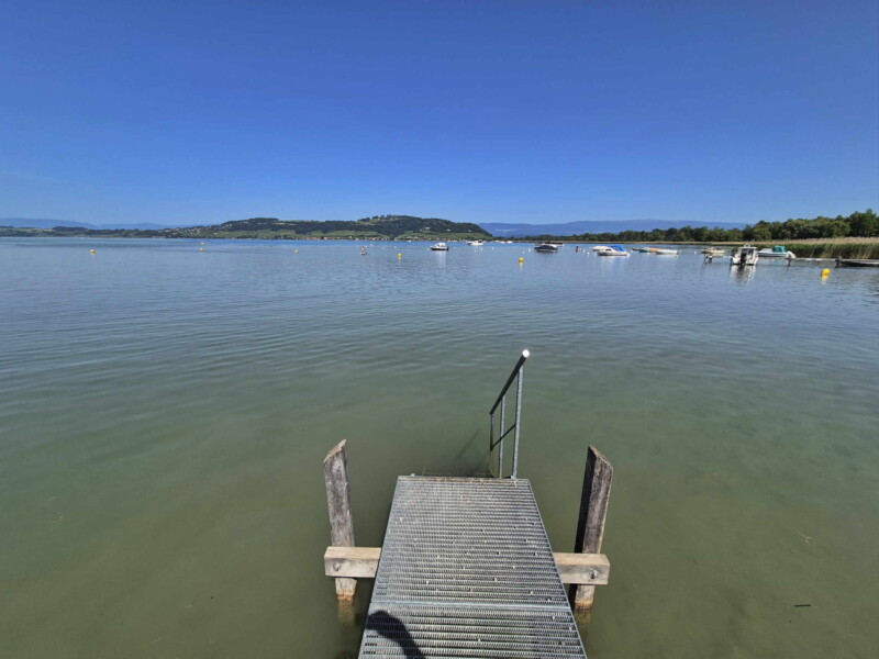 La petite zone de pelouse et les enrochements. Le petit ponton. Plage du Camping Muntelier, région Morat.