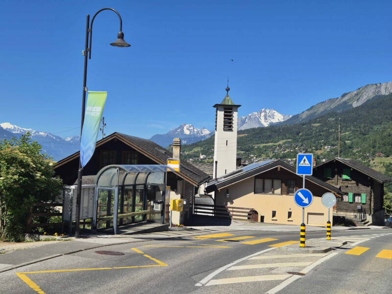 Le village d'Icogne. Au premier plan, l'arrêt du bus et la chapelle d'Icogne, placée sous la protection de Saint Grégoire de Nazianze. En arrière-plan, sur la droite, le Grand Chavalard et Haut de Cry.