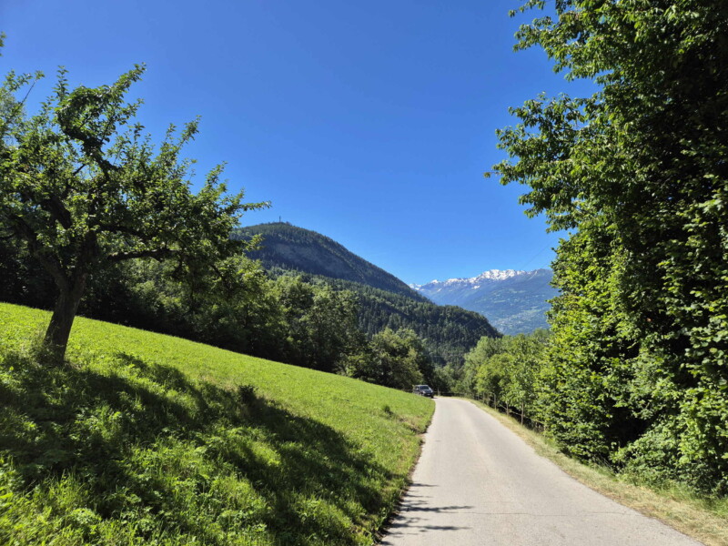 Descente à la Lienne. La route avec la colline du Châtelard en arrière-plan. Randonnée bisse de Clavau.