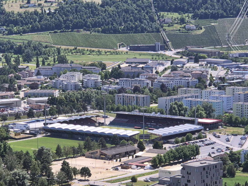 Le zoom sur le stade de Tourbillon utilisé par le Football Club de Sion. En arrière-plan, à droite, l'ancienne usine hydroélectrique de Chandoline liée au barrage de la Grande Dixence et stoppée en 2013. Randonnée bisse de Clavau.