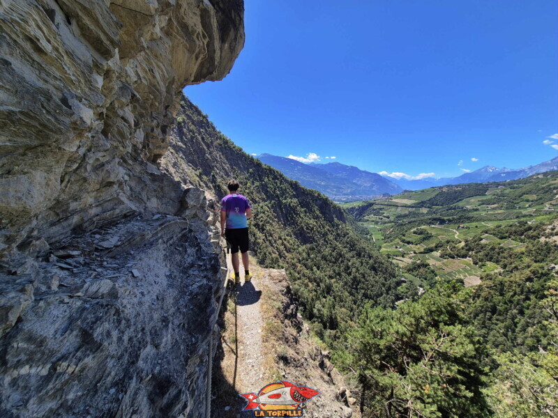 Le chemin du bisse au bord de la falaises avec des mains courantes pour se sécuriser. Sur la droite la vallée de la Lienne et son vignoble. Le chemin du bisse au bord de la falaises avec des mains courantes pour se sécuriser. Sur la droite la vallée de la Lienne et son vignoble.