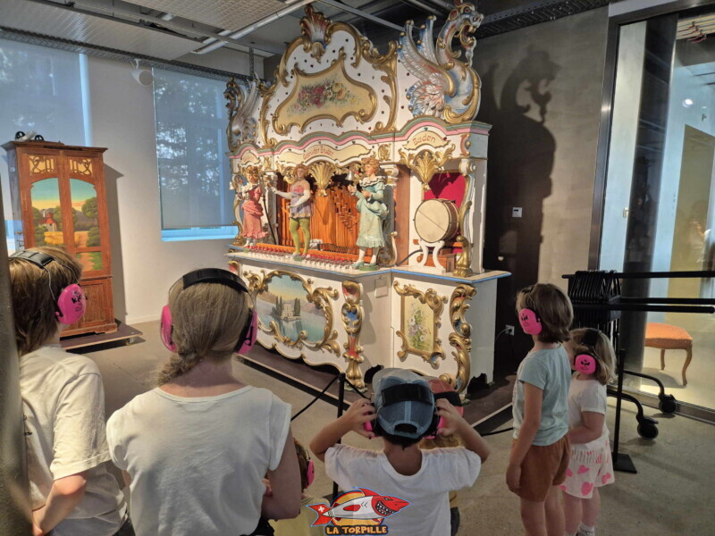 Des enfants qui écoutent une machine à musique monumentale lors de la visite guidée. Des écouteurs sont donnés aux enfants en raison du son de fort volume émis par cette machine. Des enfants qui écoutent une machine à musique monumentale lors de la visite guidée. Des écouteurs sont donnés aux enfants en raison du son de fort volume émis par cette machine. MuMAPS - Musée de la Mécanique d'Art et du Patrimoine - Sainte-Croix