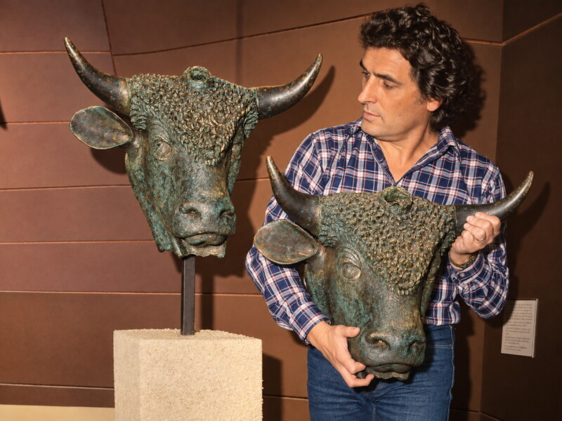 Cette photo historique immortalise un moment clé pour le patrimoine valaisan : le retour des originaux des Grands Bronzes d’Octodure de Sion à Martigny le 15 janvier 1983. On y voit Léonard Gianadda lui-même, en train de mettre en place la fameuse tête de taureau tricorne gallo-romaine sur son socle. Il fait pression auprès des autorités valaisannes pour le retour de ce joyau dans la ville où il est originaire. Léonard Gianadda pose volontairement avec la réplique dans ses mains juste à côté de l'œuvre authentique pour célébrer sa victoire culturelle. Photo colorisée à partir d'une photo présentée par la fondation Gianadda.